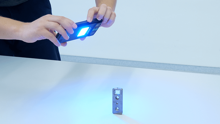 Ein Metall Gegenstand, der auf einem Tisch steht, wird von Person mit dem Scoobe3D 3D Scanner handgeführt digitalisiert. Dabei leuchtet die LED für den Scan.