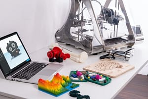 3D Drucker, 3D gedruckte Artikel und ein Laptop auf einem Tisch